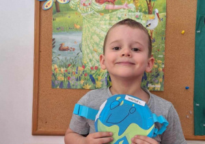 Chłopiec pozuje do zdjęcia trzymając obrazek kuli ziemskiej