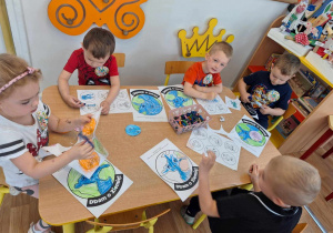 Grupa dzieci siedzi przy stole i koloruje obrazek kuli ziemskiej