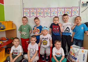 Chłopcy siedzą na dywanie i pozują do zdjęcia z solenizantem