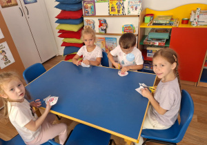 Grupa dzieci siedzi przy stoliku i wycina