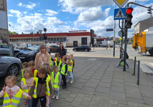 Dzieci stoją parami na chodniku i obserwują ruch uliczny