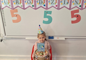 Marysia pozuje do zdjęcia, trzymając w dłoniach słodki poczęstunek dla dzieci