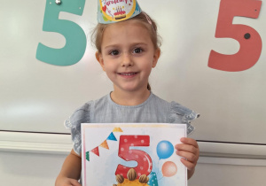 Marysia pozuje do zdjęcia, trzymając w dłoniach urodzinowy dyplom