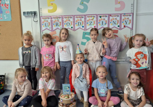 Dziewczynki stoją na dywanie i pozują z Marysią do zdjęcia