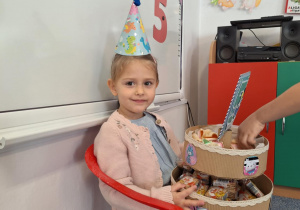 Marysia siedzi na krzesełku i częstuje dzieci słodyczami