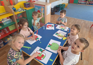 Grupa dzieci siedzi przy stoliku i wydziera papierem kolorowym kontur jabłka