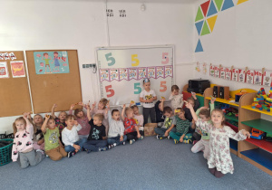 Dzieci siedzą na dywanie i pokazują trzymając w górze cukierka