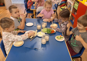 Grupa dzieci siedzi przy stoliku i robi sobie kanapki