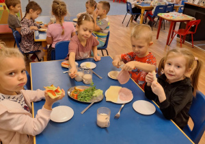 Grupa dzieci siedzi przy stoliku i robi sobie kanapki
