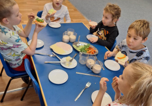 Grupa dzieci siedzi przy stoliku i robi sobie kanapki
