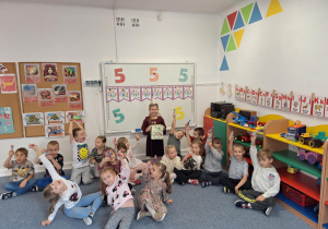 Dzieci siedzą na dywanie i pokazują trzymając w ręku cukierek od solenizantki
