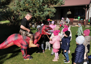 Dzieci uczestniczą w zabawie z animatorem przebranym za dinozaura