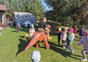 Dzieci uczestniczą w zabawie z animatorem przebranym za dinozaura