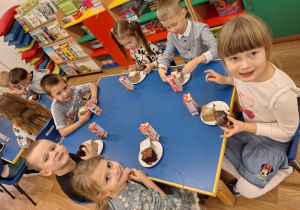 Grupa dzieci siedzi przy stoliku i spożywa poczęstunek