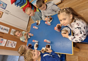 Grupa dzieci siedzi przy stoliku i spożywa poczęstunek