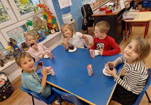 Grupa dzieci siedzi przy stoliku i spożywa poczęstunek