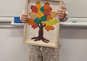 Dziewczynka pokazuje wykonane przez siebie jesienne drzewo