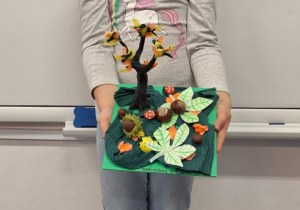 Dziewczynka pokazuje wykonane przez siebie jesienne drzewo