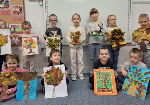 Grupa dzieci pozuje do zdjęcia z wykonanymi przez siebie jesiennymi drzewami