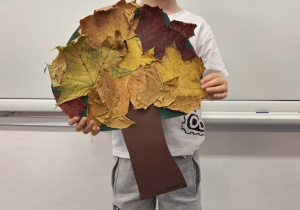 Chłopiec pokazuje wykonane przez siebie jesienne drzewo