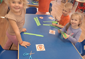 Grupa dzieci siedzi przy stoliku i wykonuje prace plasyczną