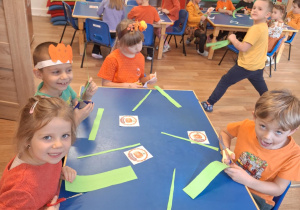 Grupa dzieci siedzi przy stoliku i wykonuje prace plasyczną