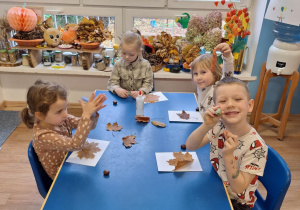 Grupa dzieci siedzi przy stoliku i wykonuje pracę plastyczną