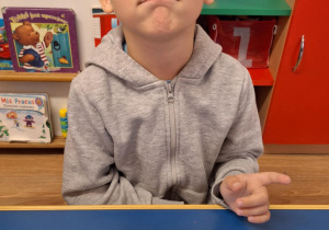 Chłopiec siedzi przy stole i pokazuje swoją prace plastyczną