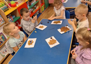 Grupa dzieci siedzi przy stoliku i wykonuje pracę plastyczną