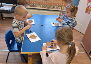 Grupa dzieci siedzi przy stoliku i wykonuje pracę plastyczną