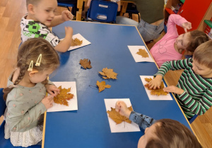 Grupa dzieci siedzi przy stoliku i wykonuje pracę plastyczną