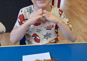 Chłopiec siedzi przy stole i pokazuje swoją prace plastyczną