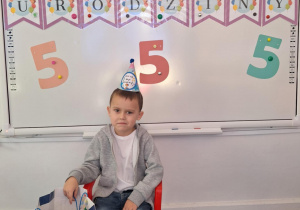 Wojtek siedząc na krześle, pozuje do zdjęcia trzymając torbę ze słodyczami