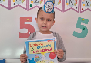 Wojtek pozuje do zdjęcia, trzymając w dłoniach urodzinowy dyplom