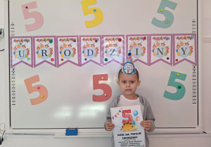 Wojtek pozuje do zdjęcia, trzymając w dłoniach urodzinowy dyplom