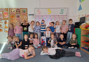 Cała grupa dzieci stoi na dywanie i pozuje do zdjęcia z Wojtkiem