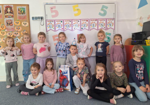 Grupa dziewczynek stoi na dywanie i pozuje do zdjęcia z Wojtkiem