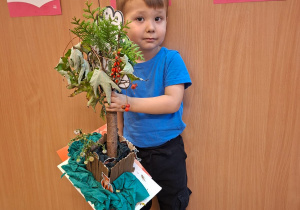 Dziecko pozuje do zdjęcia z pracą wykonaną wspólnie z rodzicami