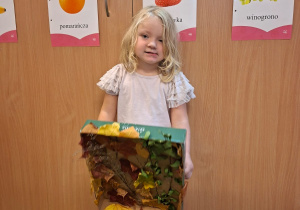 Dziecko pozuje do zdjęcia z pracą wykonaną wspólnie z rodzicami