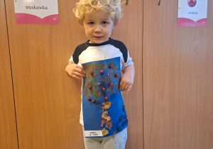 Dziecko pozuje do zdjęcia z pracą wykonaną wspólnie z rodzicami