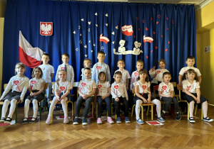 Grupa dzieci w odświętnych strojach z kotylionami na piersi