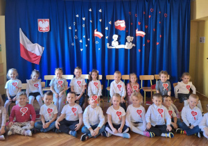 Dzieci siedzą i pozują do zdjęcia na tle dekoracji z okazji Narodowego Święta Niepodległości