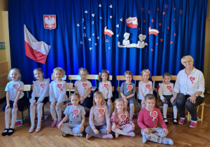 Dziewczynki siedzą i pozują do zdjęcia na tle dekoracji z okazji Narodowego Święta Niepodległości