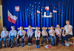 Chłopcy siedzą i pozują do zdjęcia na tle dekoracji z okazji Narodowego Święta Niepodległości