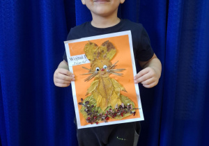 Chłopiec stoi i trzyma w rękach prace plasyczną