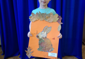 Chłopiec stoi i trzyma w rękach prace plasyczną