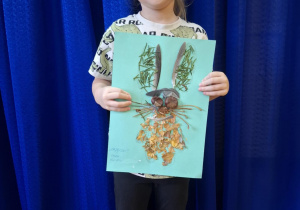 Dziewczynka stoi i trzyma w rękach prace plasyczną