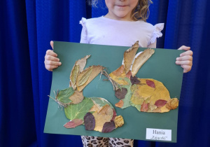 Dziewczynka stoi i trzyma w rękach prace plasyczną