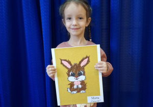 Dziewczynka stoi i trzyma w rękach prace plasyczną