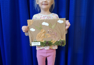 Dziewczynka stoi i trzyma w rękach prace plasyczną